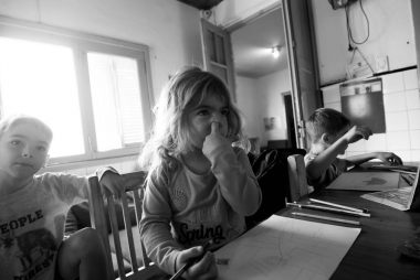Three children drawing at a table in grayscale, indoors, natural light.